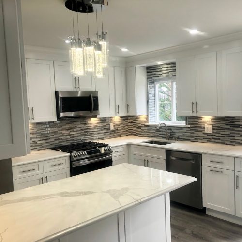 A modern kitchen featuring white cabinets and a sleek marble countertop, creating a bright and elegant atmosphere.