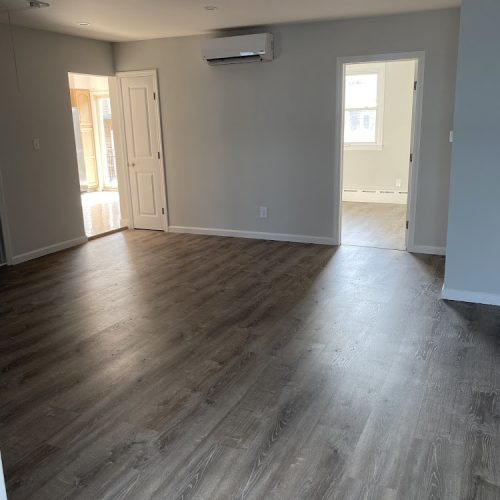 A vacant living room featuring wooden floors and gray walls, creating a minimalist and spacious atmosphere.