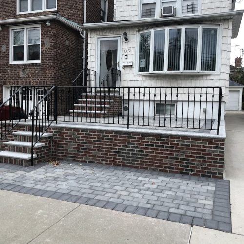 A brick patio featuring a decorative wrought iron railing, showcasing a blend of rustic and elegant design elements.