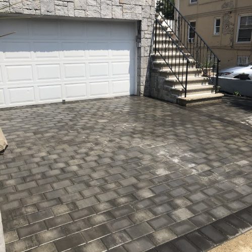 A driveway featuring elegant brick pavers, complemented by a set of stairs leading to an entrance.